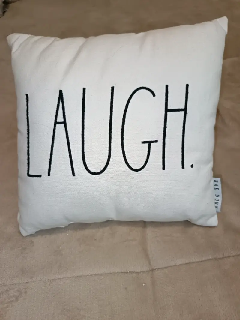 Cojín decorativo blanco con texto 'Laugh'