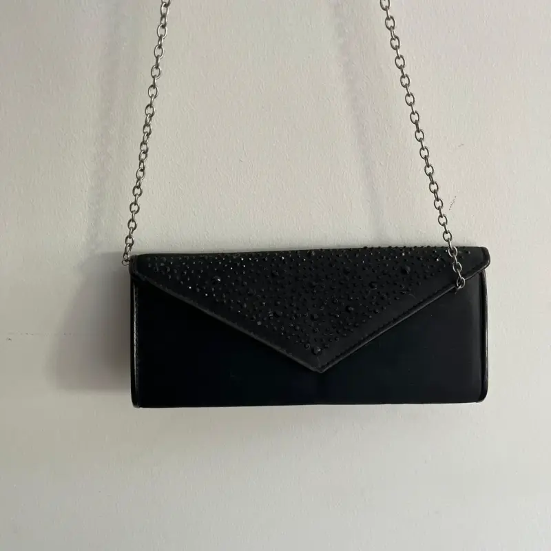 Cartera de mano negra con cadena y detalles brillantes
