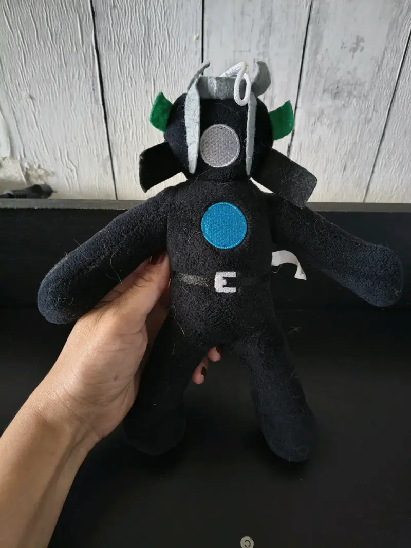 Peluche de personaje negro con detalles coloridos