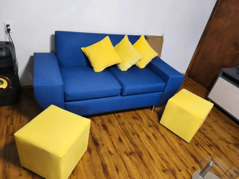 Sofá azul con cojines y pufs amarillos - 1
